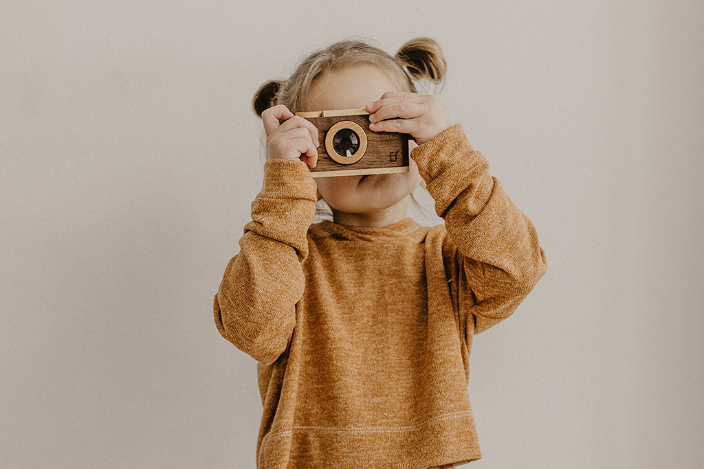 Toddler holding the wooden toy camera up to her eyes